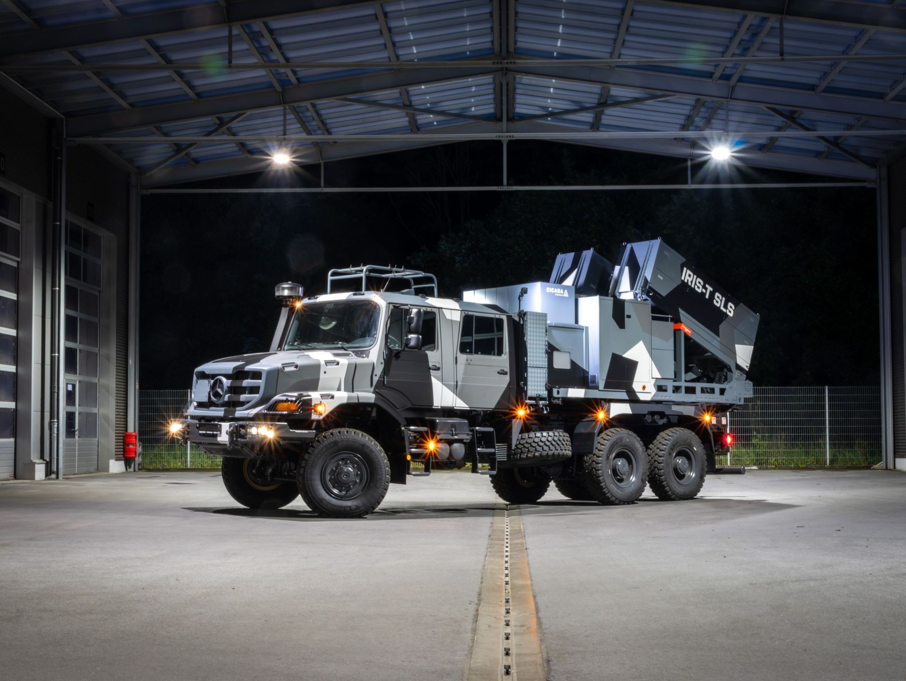 Armored military vehicle with IRIS-T SLS missile system, parked in a well-lit hangar during nighttime.