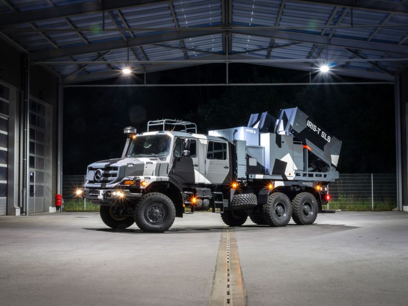 Armored military vehicle with IRIS-T SLS missile system, parked in a well-lit hangar during nighttime.