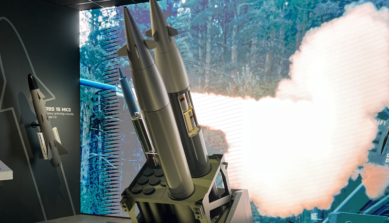 Ausstellung von Raketen, mit einem digitalen Bildschirm, auf dem ein Raketenstart und Rauch zu sehen sind.