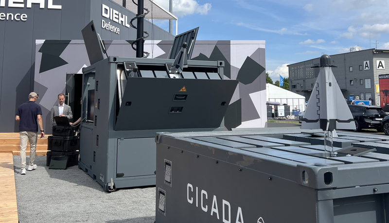 Ausstellung von militärischer Verteidigungsausrüstung im Freien und ein Container mit der Aufschrift „CICADA“.