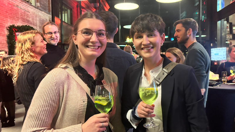 Zwei Frauen mit grünen Getränken in der Hand lachen fröhlich.