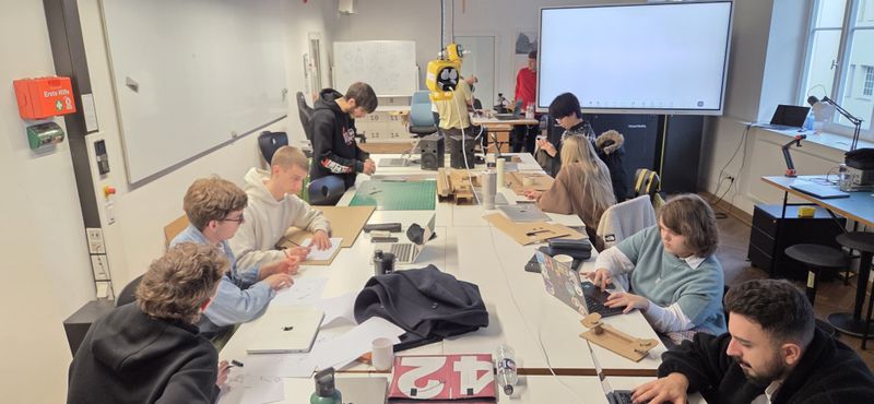 Die Studenten sitzen gemeinsam am Tisch und arbeiten am Laptop.