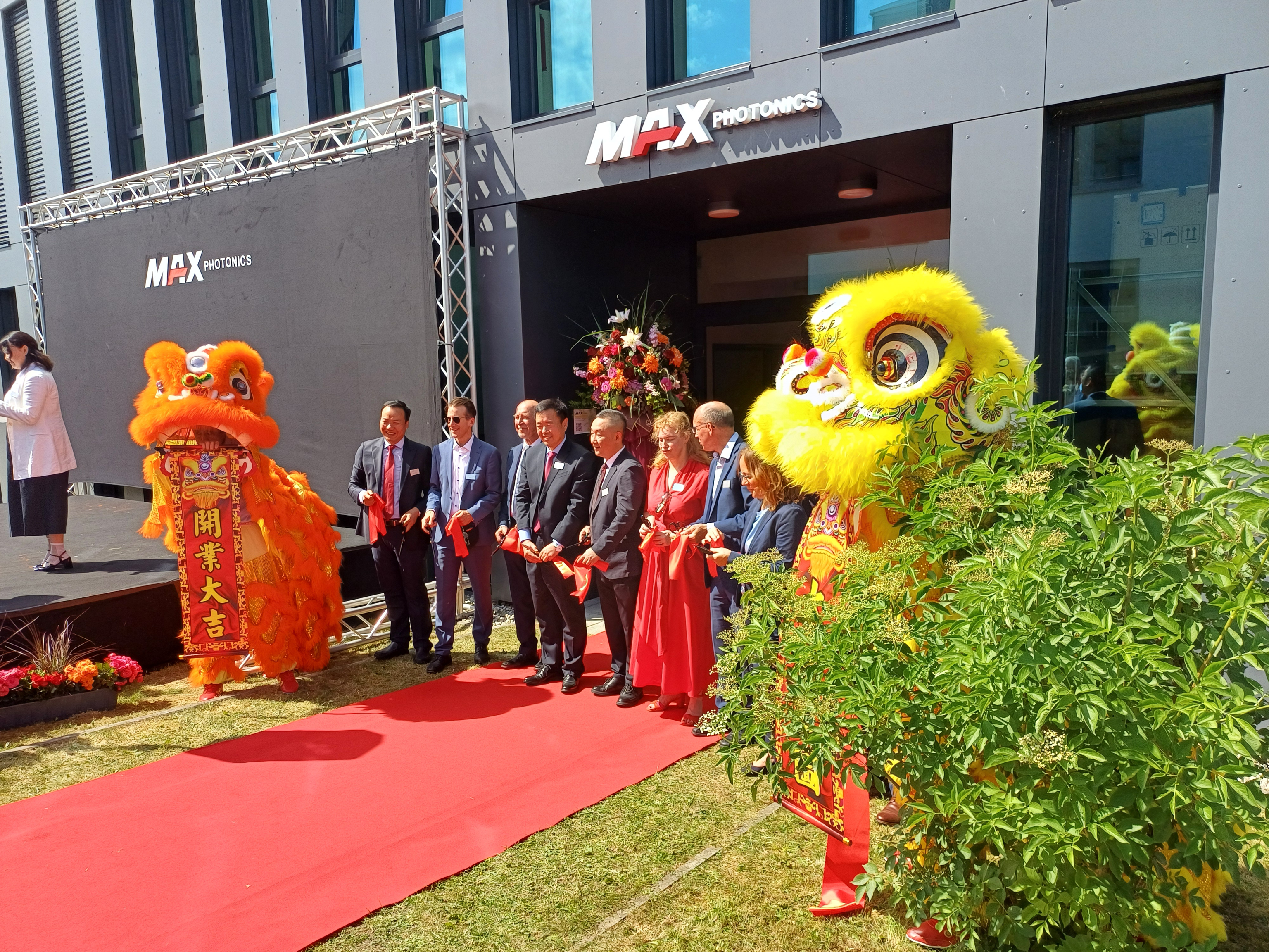 Several people are standing on a red carpet, two of them wearing Chinese dragon costumes.