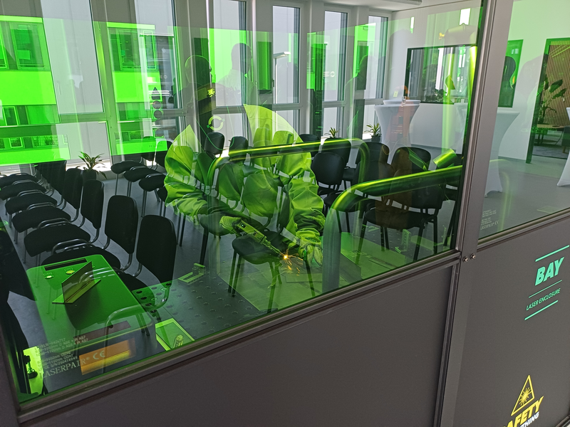 Person behind green glass demonstrating laser welding.