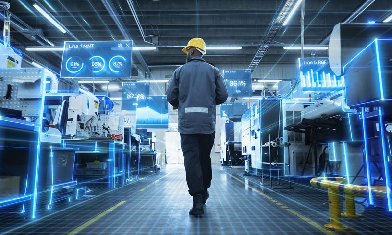 Ein Arbeiter mit Schutzhelm geht durch eine Hightech-Fabrik, in der holografische Datenanzeigen die Kennzahlen der Produktionslinie hervorheben.