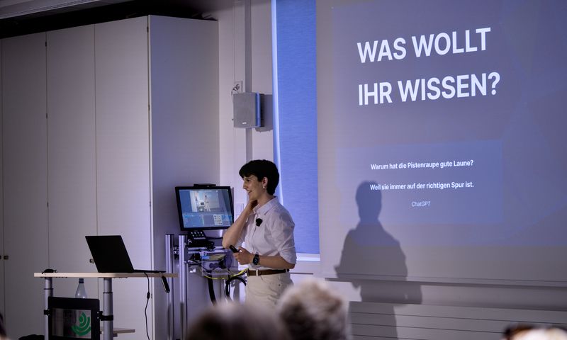 Eine Person hält in einem Seminarraum vor einer Leinwand einen Vortrag; daneben stehen ein Laptop und ein Monitor.