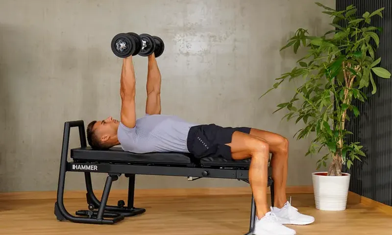 Person macht ein einem Fitness Gerät Übungen mit Hanteln.