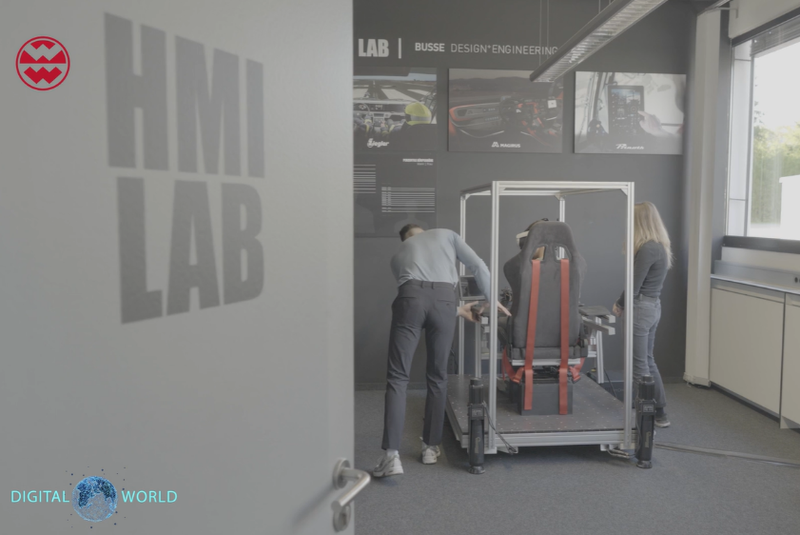 People working in a lab labeled "HMI Lab," with a setup involving a chair and metal structure, surrounded by automotive design displays.