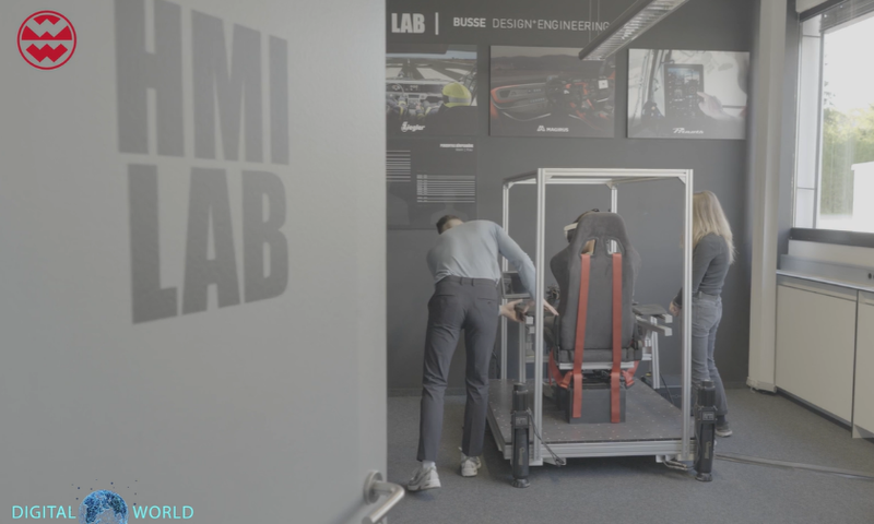 People working in a lab labeled "HMI Lab," with a setup involving a chair and metal structure, surrounded by automotive design displays.