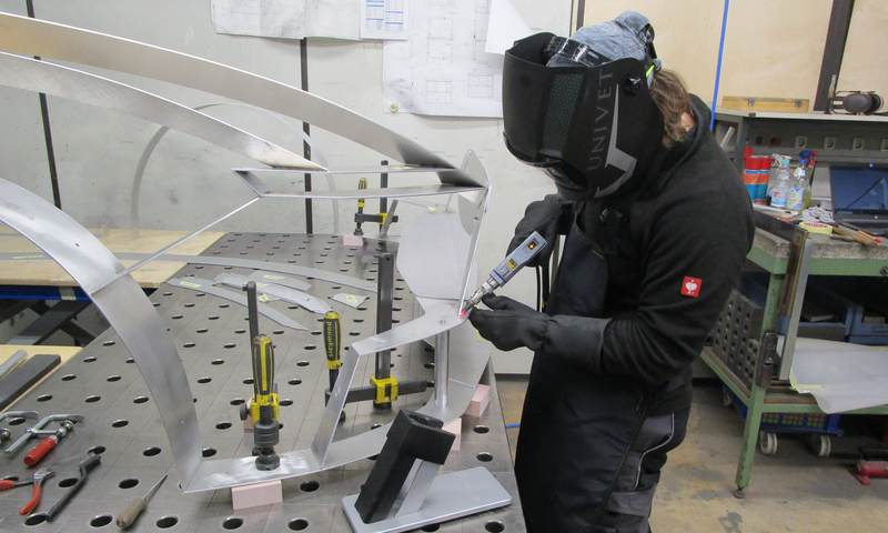 Man wearing a protective mask processes a material part using laser welding.