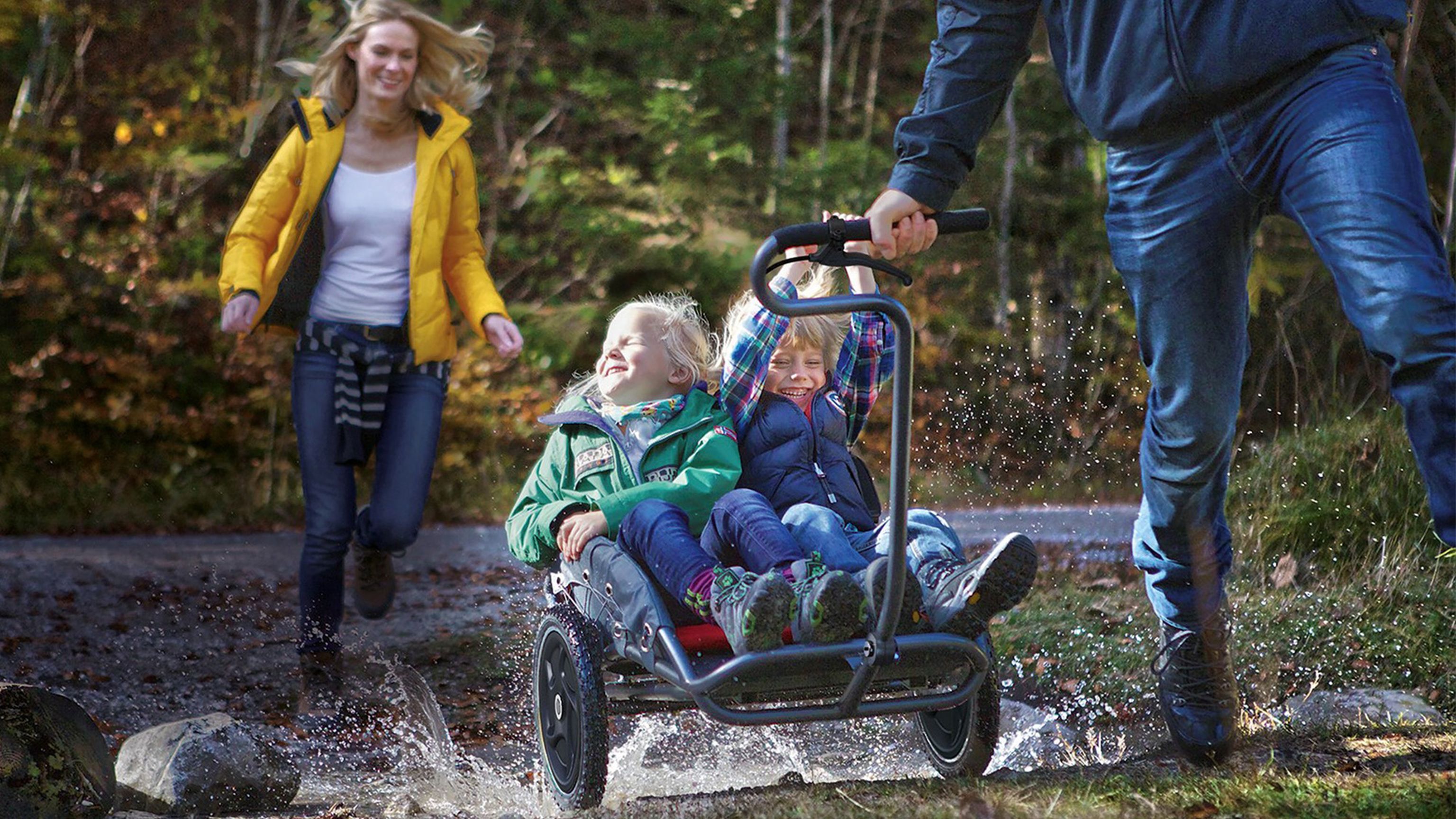 Zwei Kinder sitzen im Kinderwagen welcher durch den Wald gezogen wird