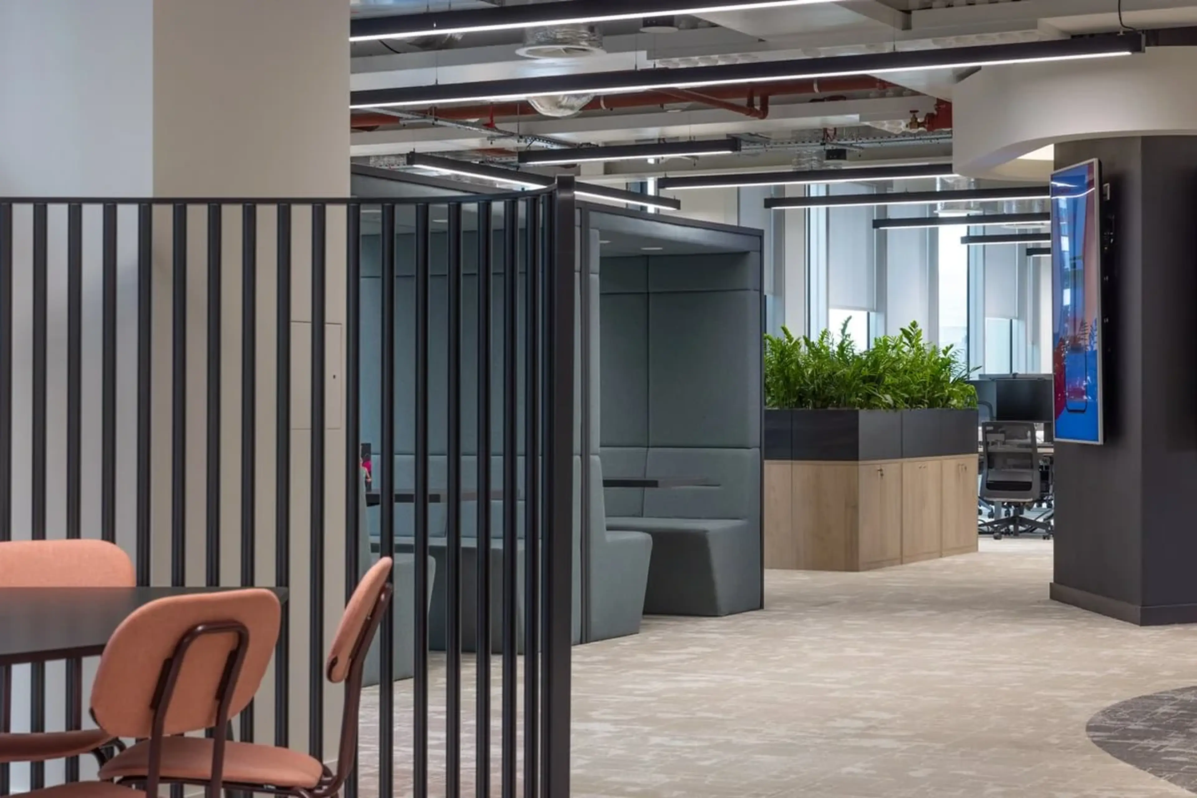 Modern office space with seating areas, a partition, and greenery. Neutral colors and open layout create a welcoming environment.
