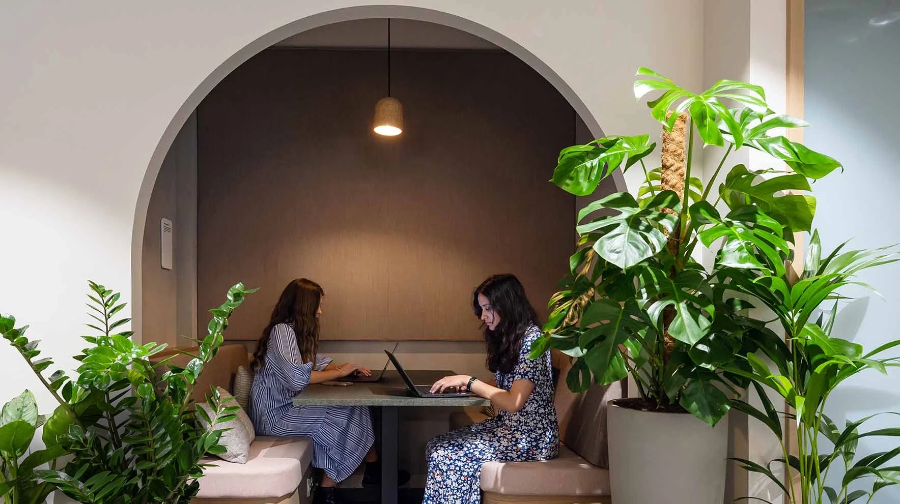 Collaborative workspace design with two people working in arched booth seating surrounded with plants