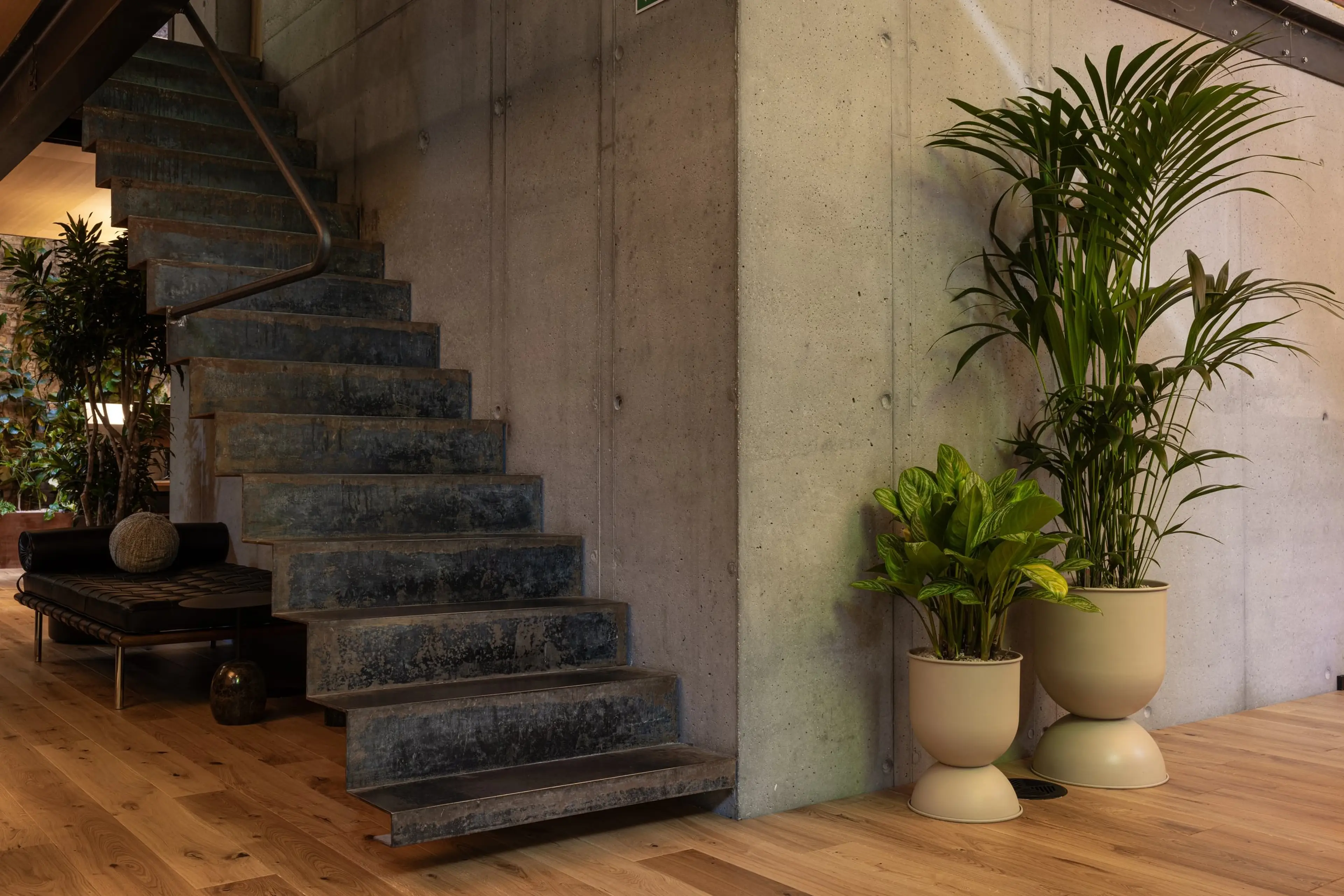 Modern interior with a concrete staircase, wooden floor, and potted plants. A bench and decorative items are placed nearby.