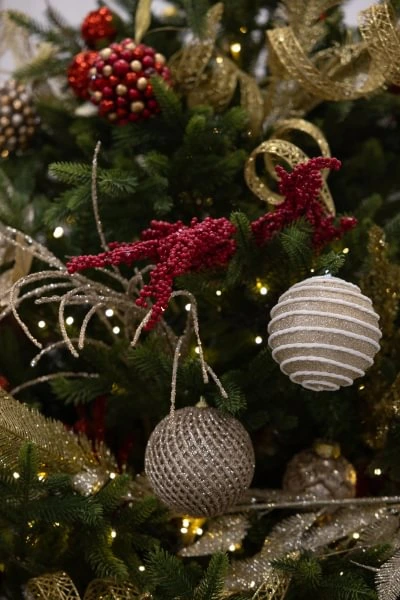 Christmas tree decorated with red berries, gold ribbons, and glittering gold ornaments, surrounded by glowing lights.