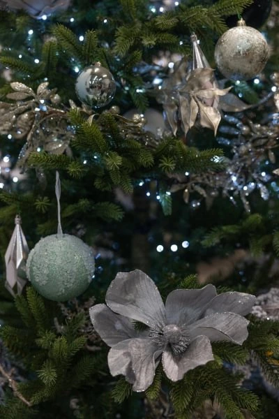 A decorated Christmas tree with silver and green ornaments, including a large metallic flower and geometric shapes, lit by small white lights.