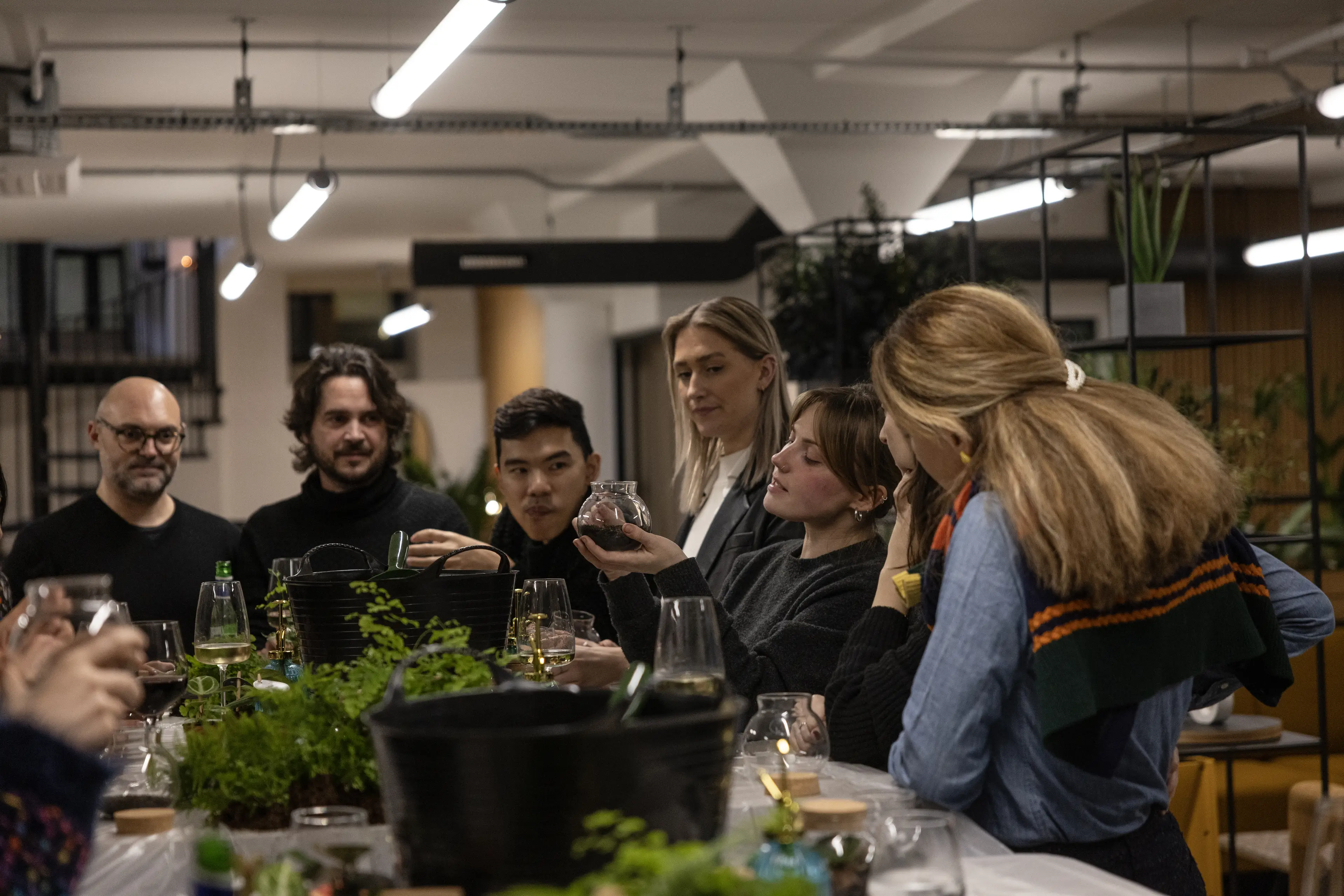 People gathered around a plant covered table, engaging in a terrarium making workshop