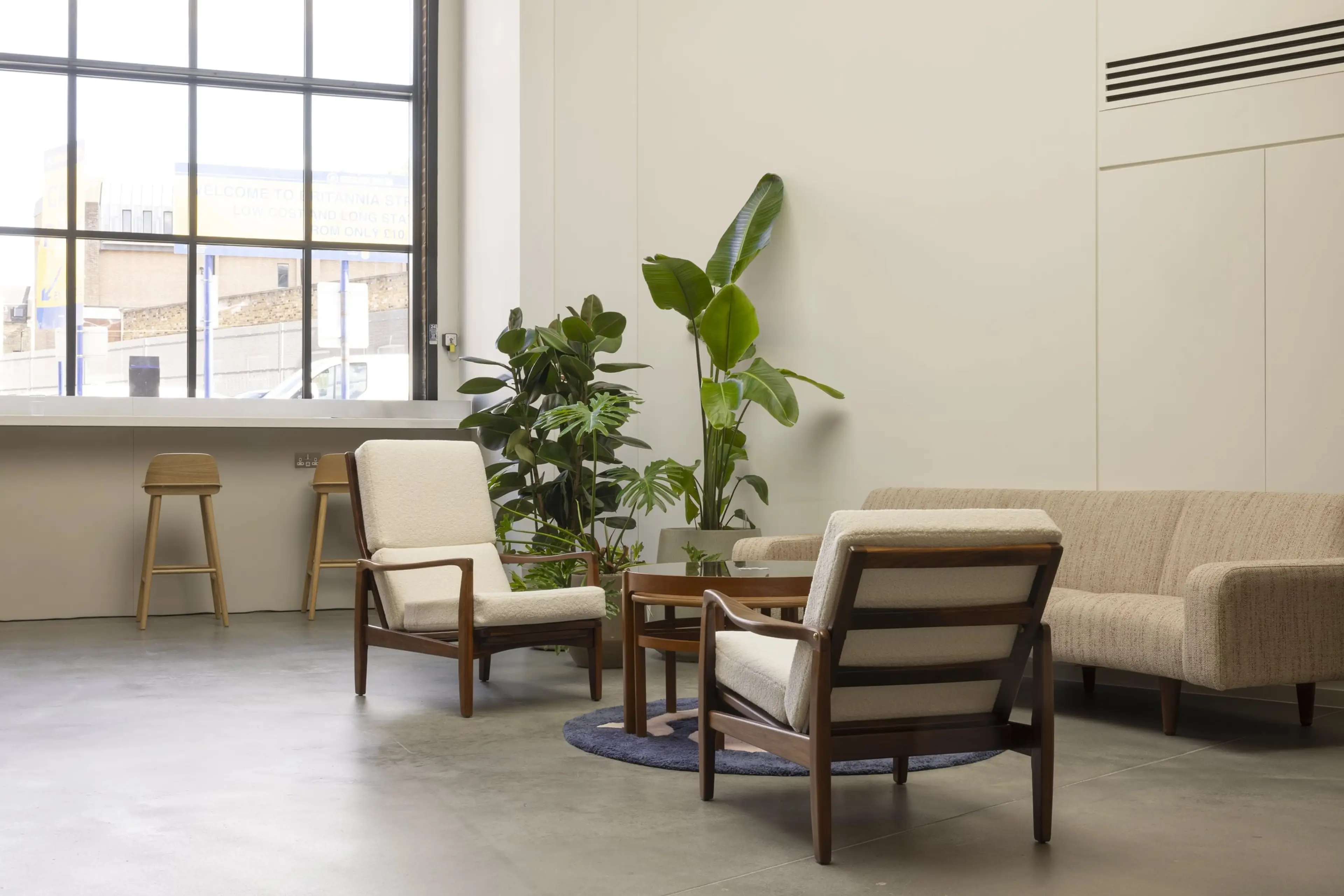An office breakout space with sofas, a big open window in the background, and office plants in the corner