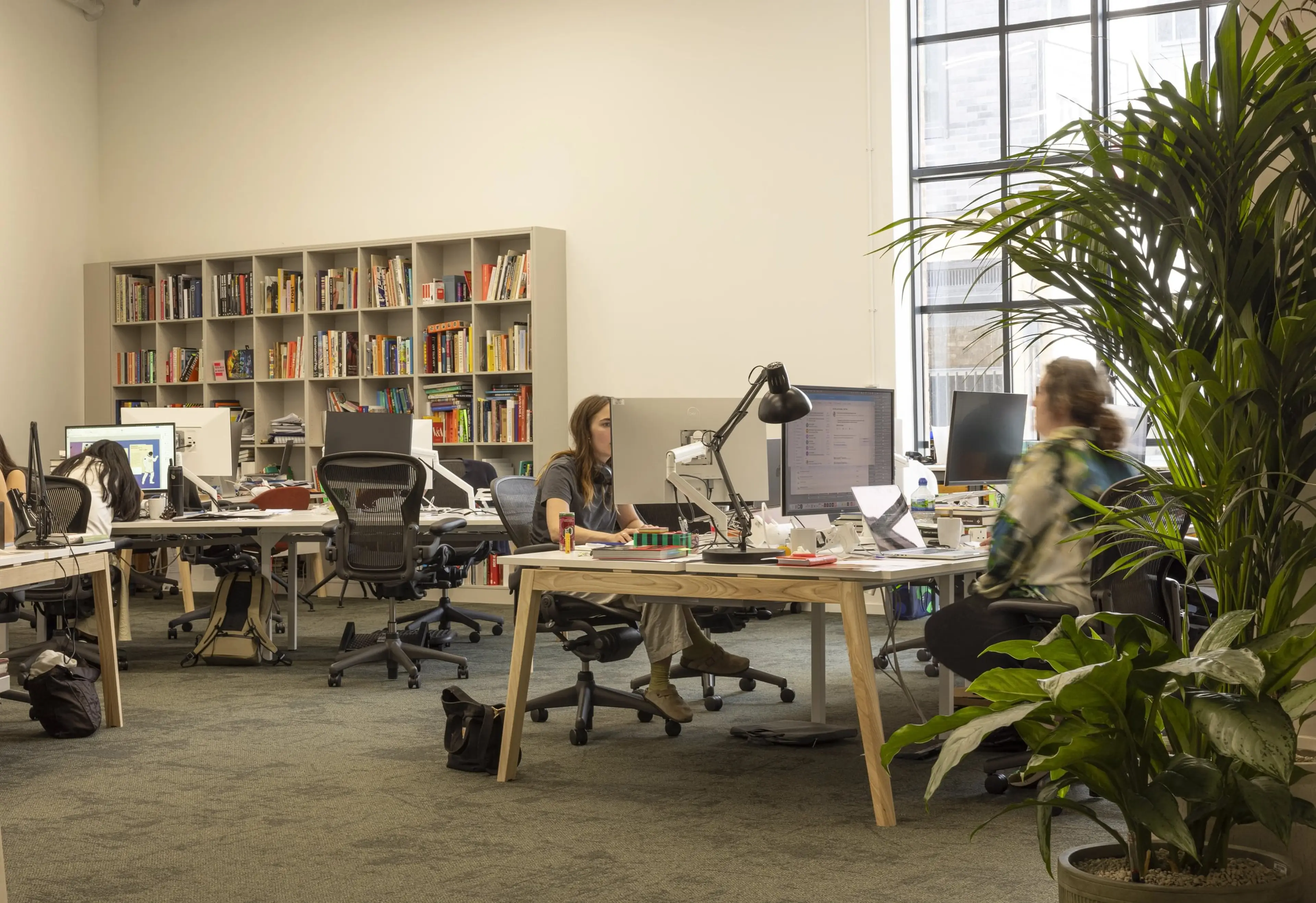 A publishers brightly lit office with a bookcase in the background, and workers at desks.