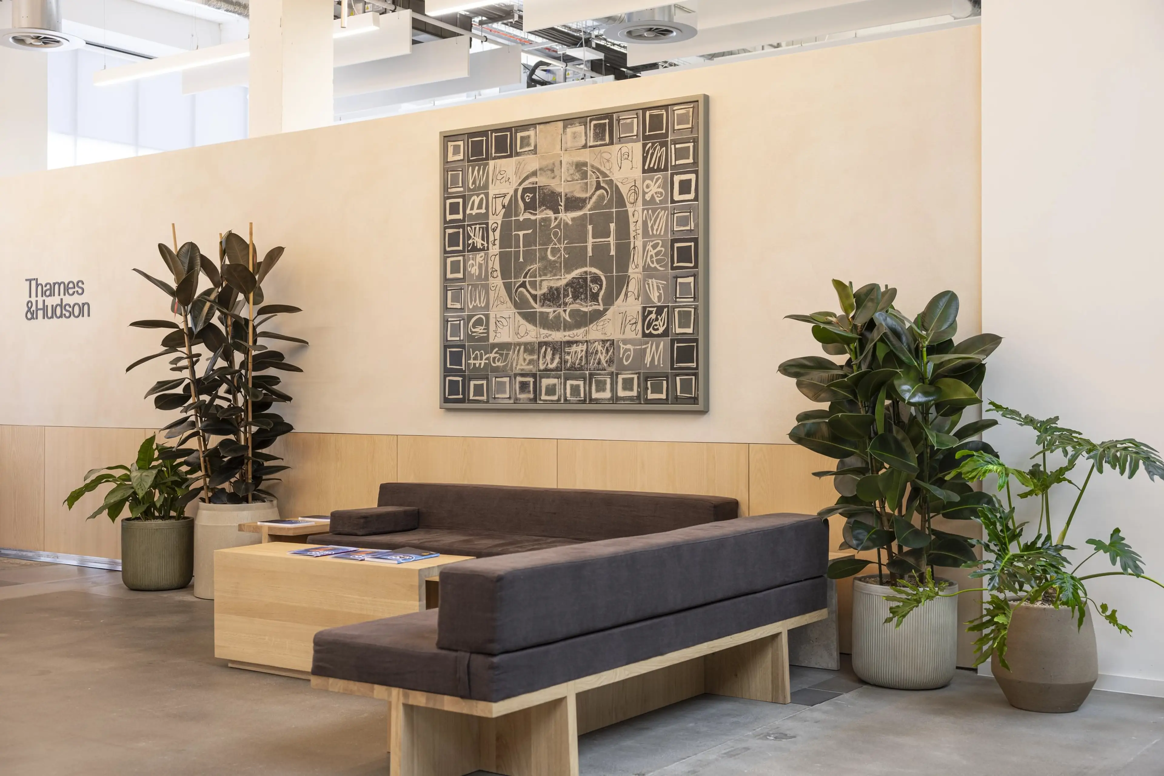 A T&H wall mural, behind a relaxing office breakout space, with indoor office plants on either side.