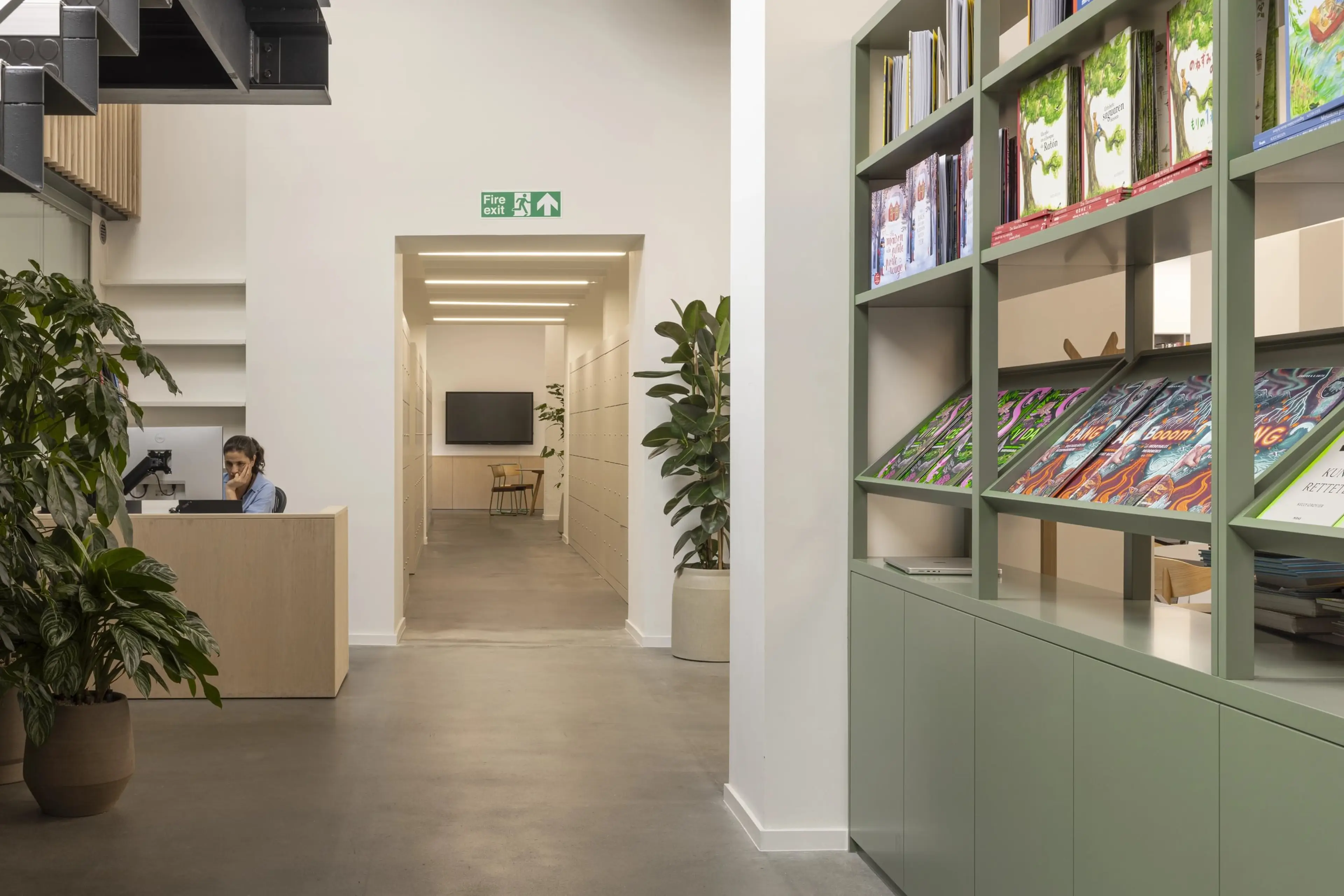 The hallway of a publishers office. Brightly lit with a bookshelf on the right hand side.