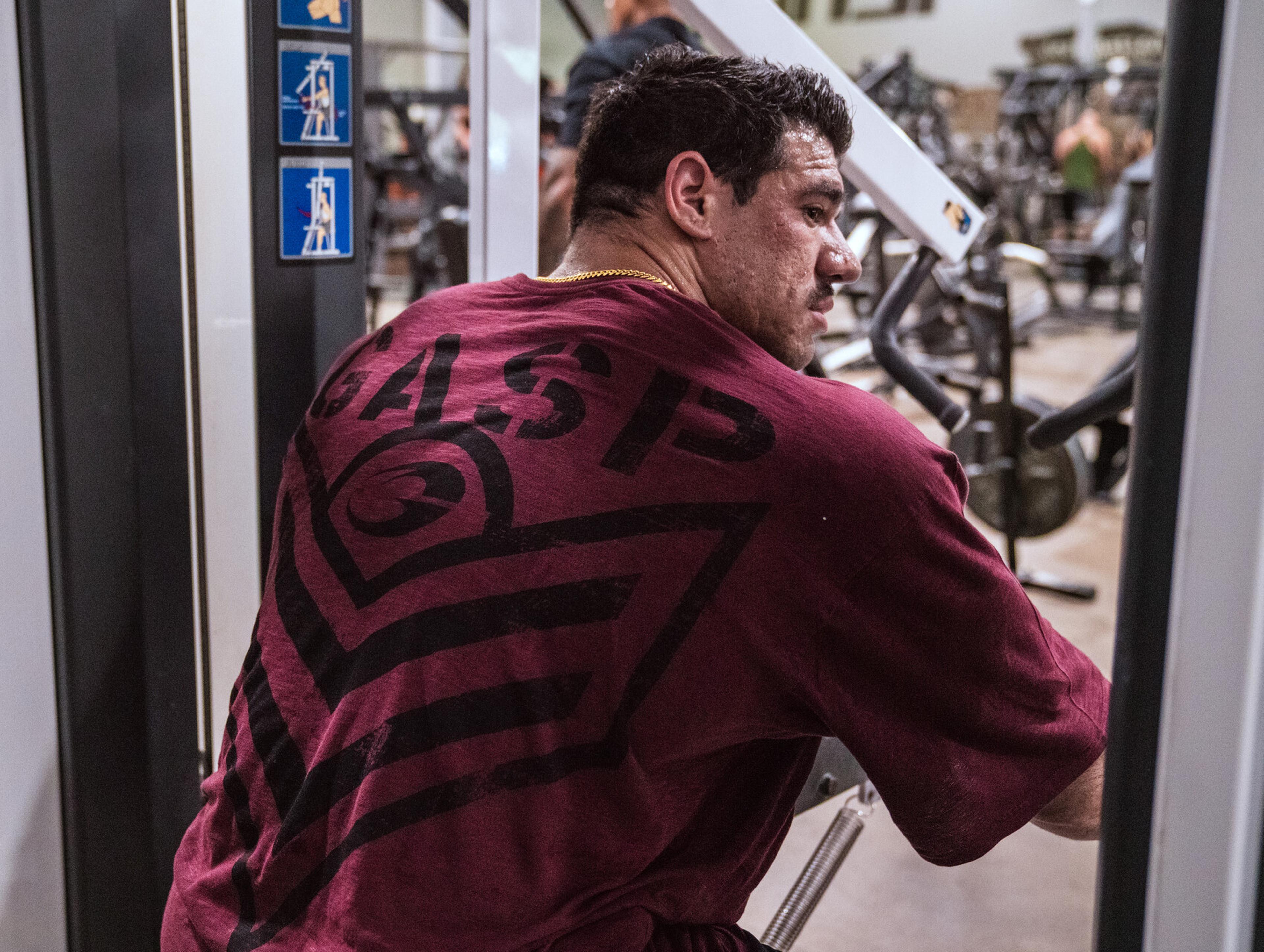 Man in a maroon "GASP" shirt using gym equipment, focused on workout, with gym setting in the background.