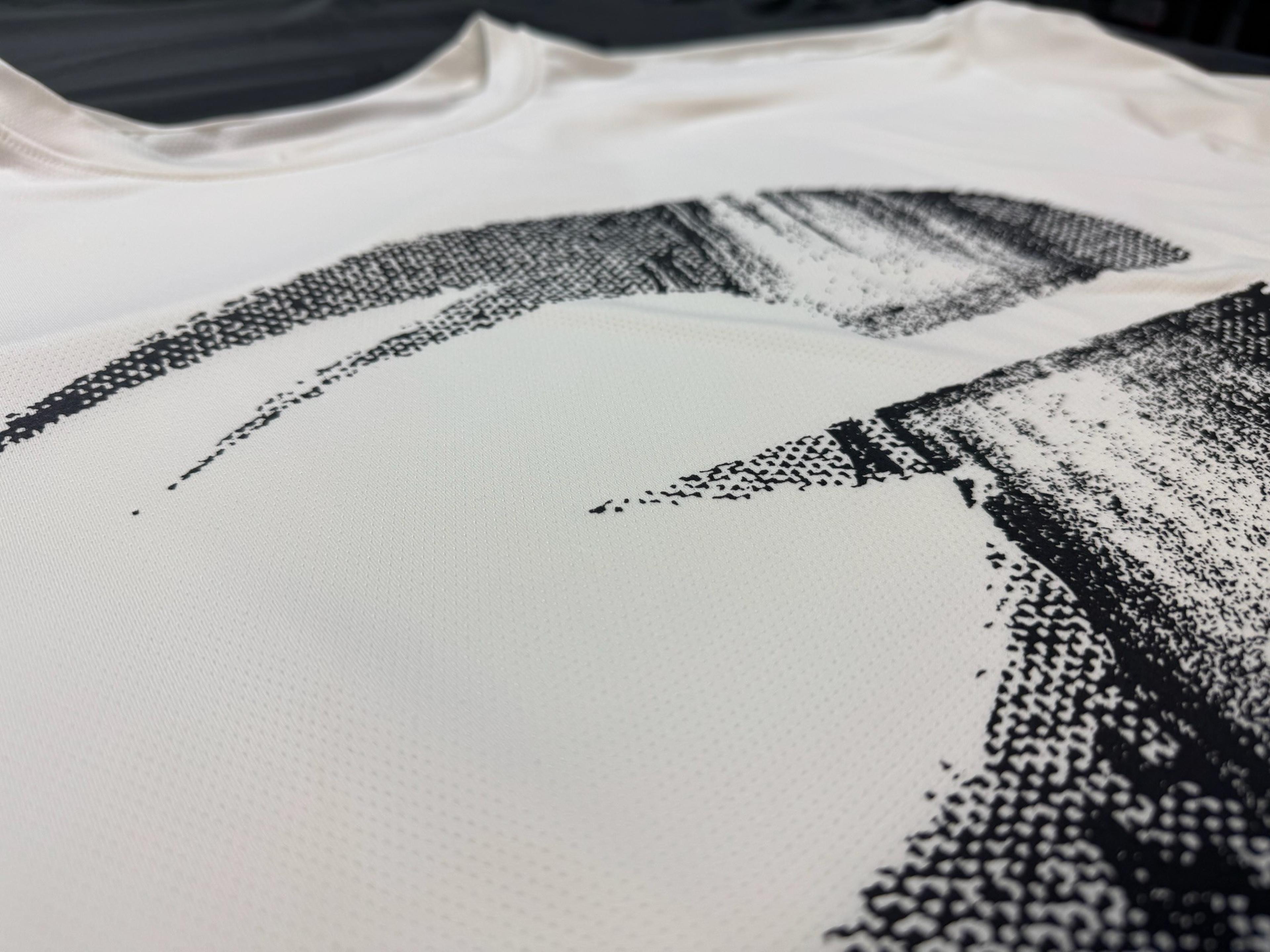 Close-up of a white shirt with a black, abstract, dotted design. The fabric has a smooth texture and a slightly glossy finish.