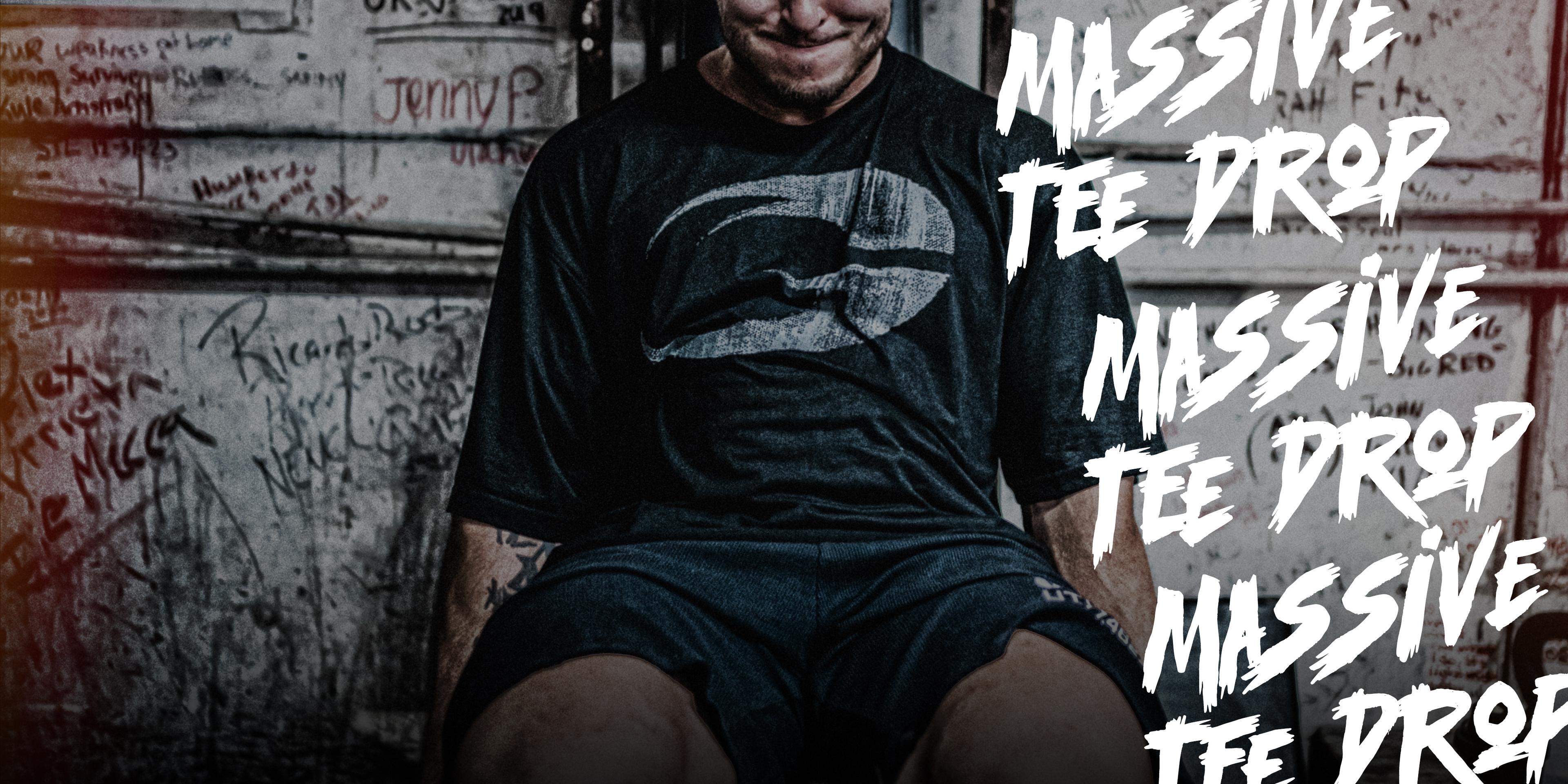 Man in a black t-shirt and shorts sits against a graffiti-covered wall with "Massive Tee Drop" text overlayed multiple times.