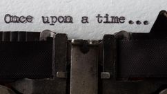 Close-up of a typewriter typing "Once upon a time..." on white paper, with visible typebars and ribbon.