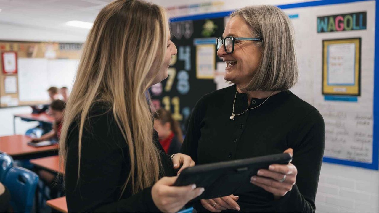 Two teachers chatting in a classroom holding an iPad.
