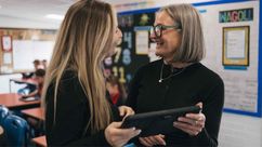 Two teachers chatting in a classroom holding an iPad.