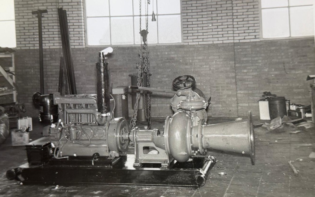 Eerste HK pomp met dieselmotor Een oude foto van een pomp met daarachter een motor in een werkplaats