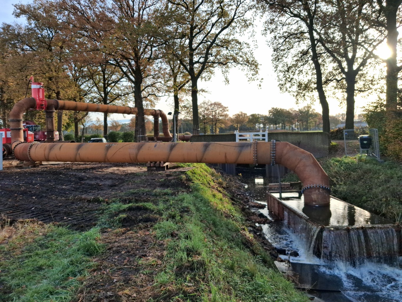 Stalen leiding met bochten en stromend water in een bosrijke omgeving.
