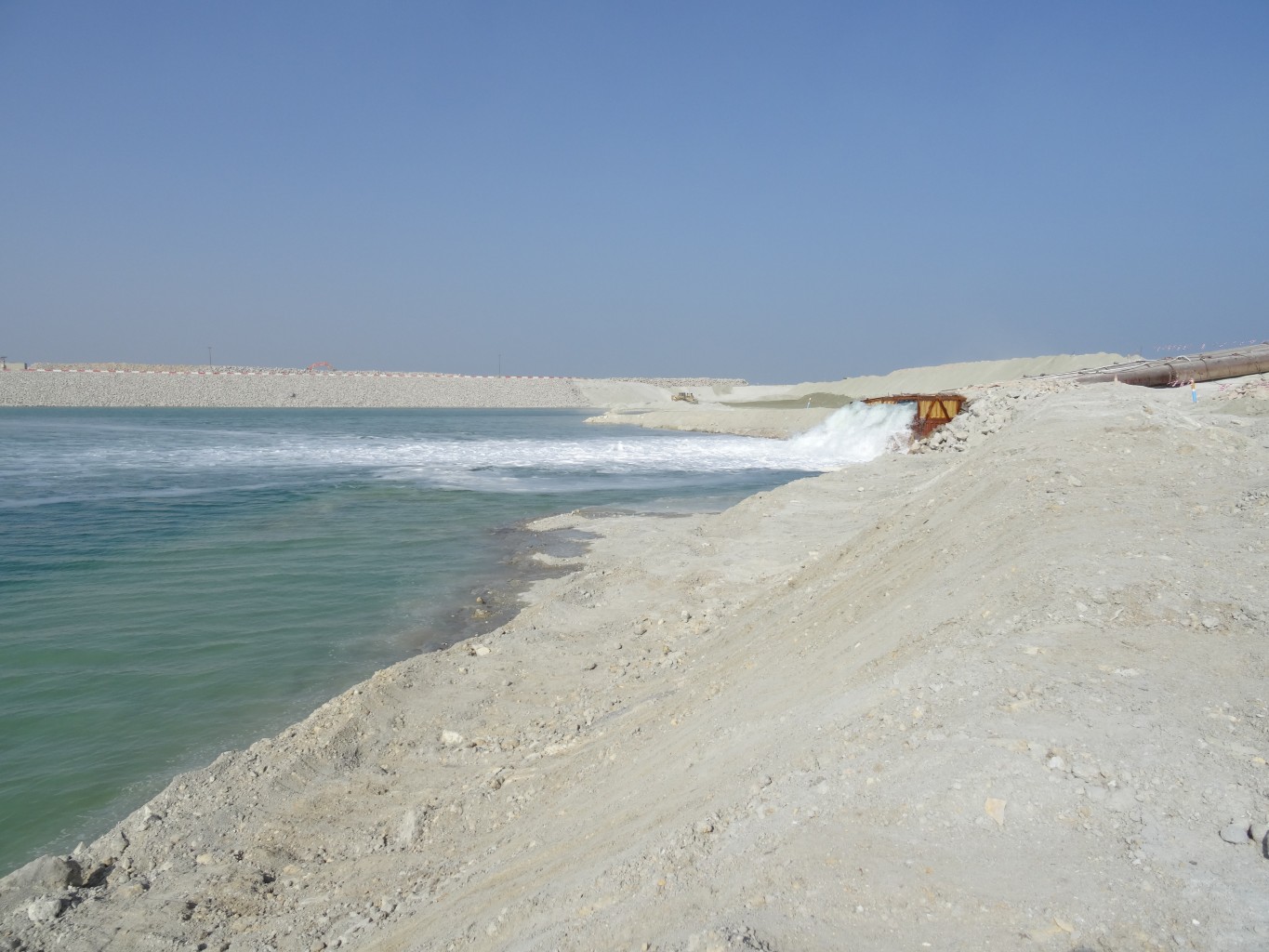 Hevelinstallatie loost water in een meer in een zanderige omgeving onder een blauwe lucht