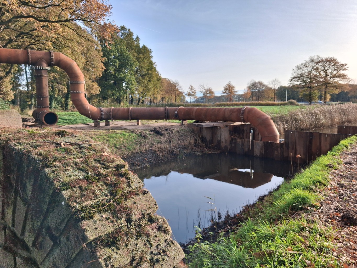 Hevel uitstroom in de GWW uitrsoom van Hevelinstallatie met bochten en wegoverspanning in een natuurlijke omgeving met op de voorgrond een gemetselde muur