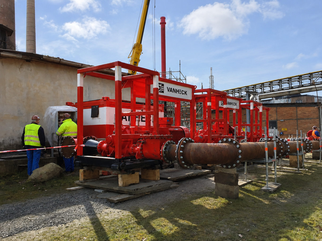 Brandblusinstallatie Drie rode pompen met leidingwerk op een industrieel terrein met twee monteurs die bij een elektrische kast staan.