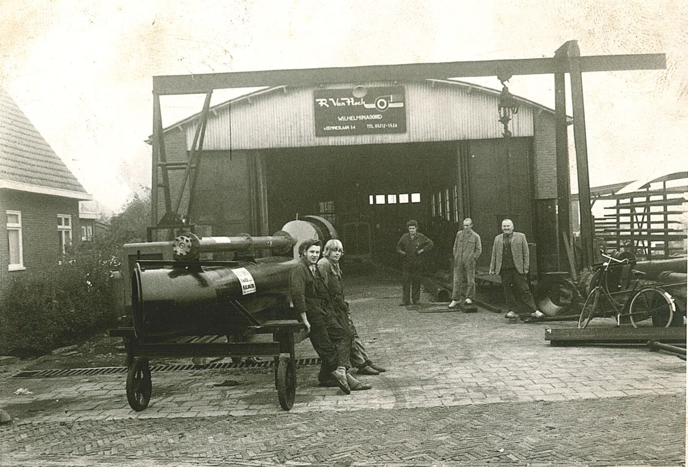 Beginjaren Van Heck Oude foto met personeel en een loods, op de voorgrond is een trekkerschroefpomp op wielen te zien