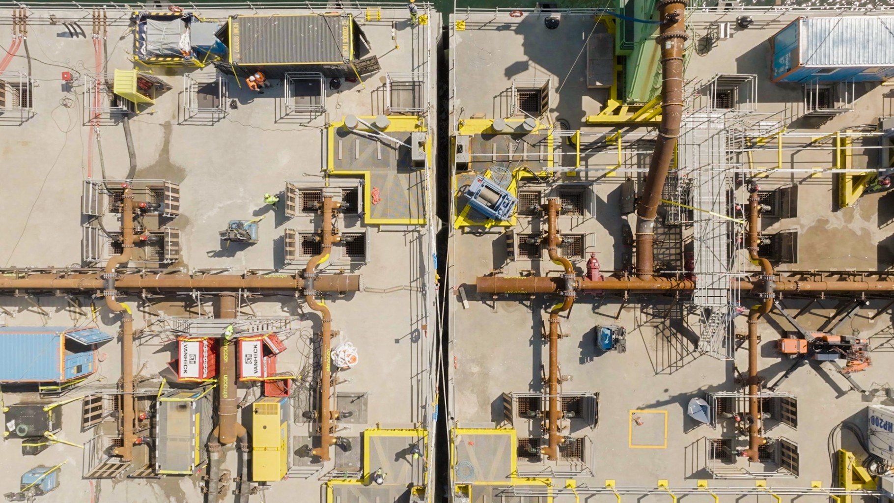 Luchtfoto van een industriële locatie met verschillende pijpleidingen, machines en containers, georganiseerd in een symmetrisch patroon.