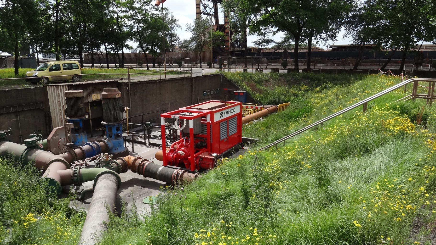 Rode waterpomp in een verdiept landschap met leidingen en een groen talud