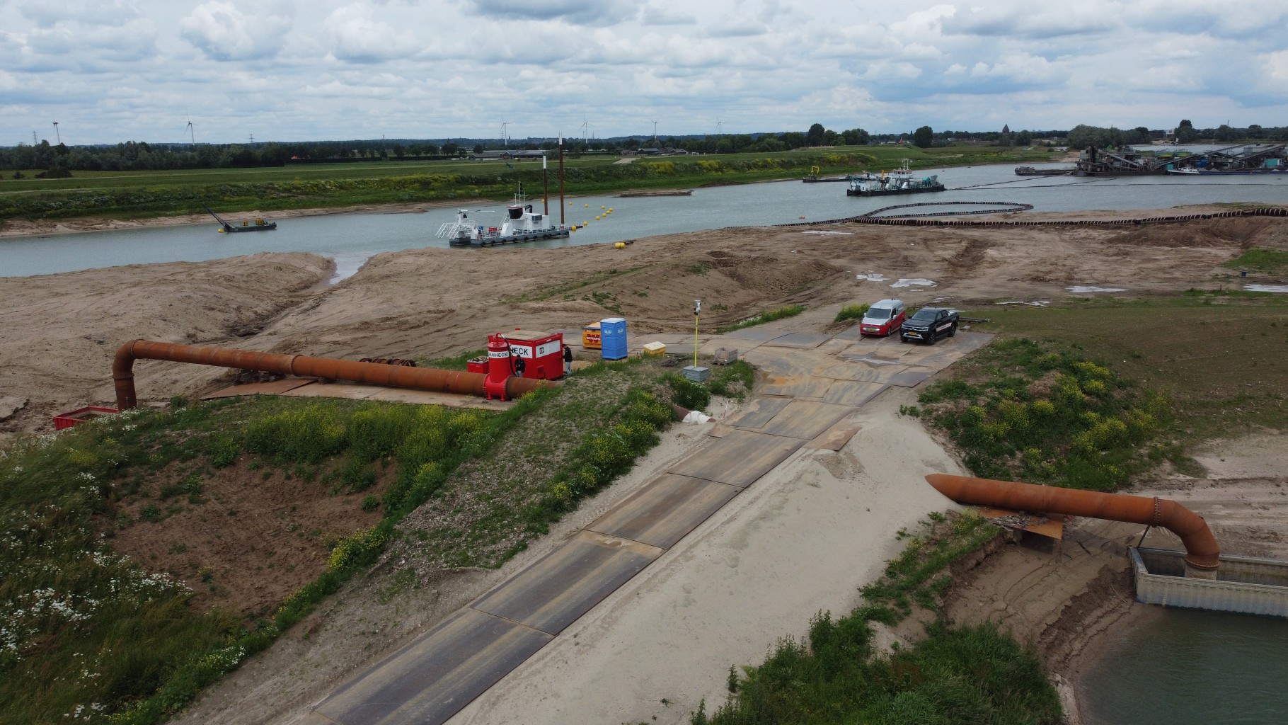 Luchtfoto van een meer met twee boten. op de voorgrond een stuk leidingwerk dat door een dijk heen loopt