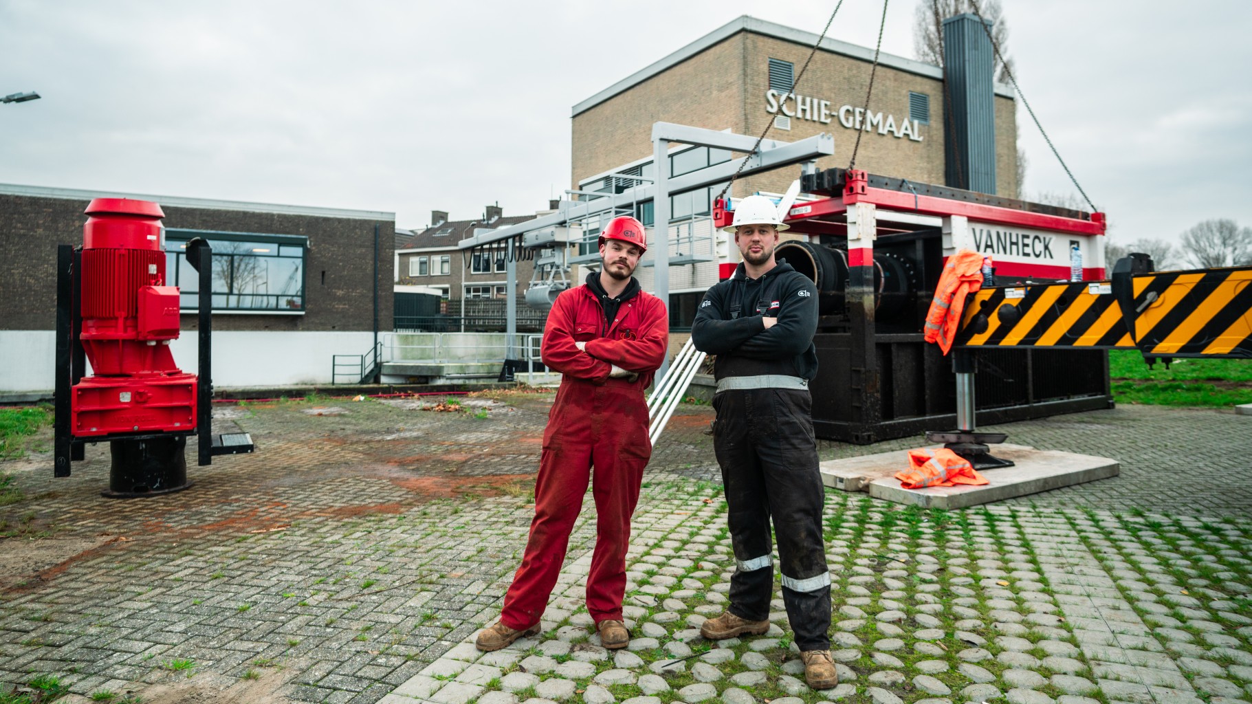 Twee monteurs poseren voor een waterpomp, elektromotor en een gemaal.