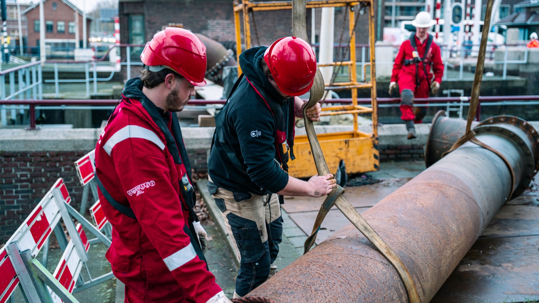 Drie monteurs aan het werk met leidingwerk in de omgeving van een sluis