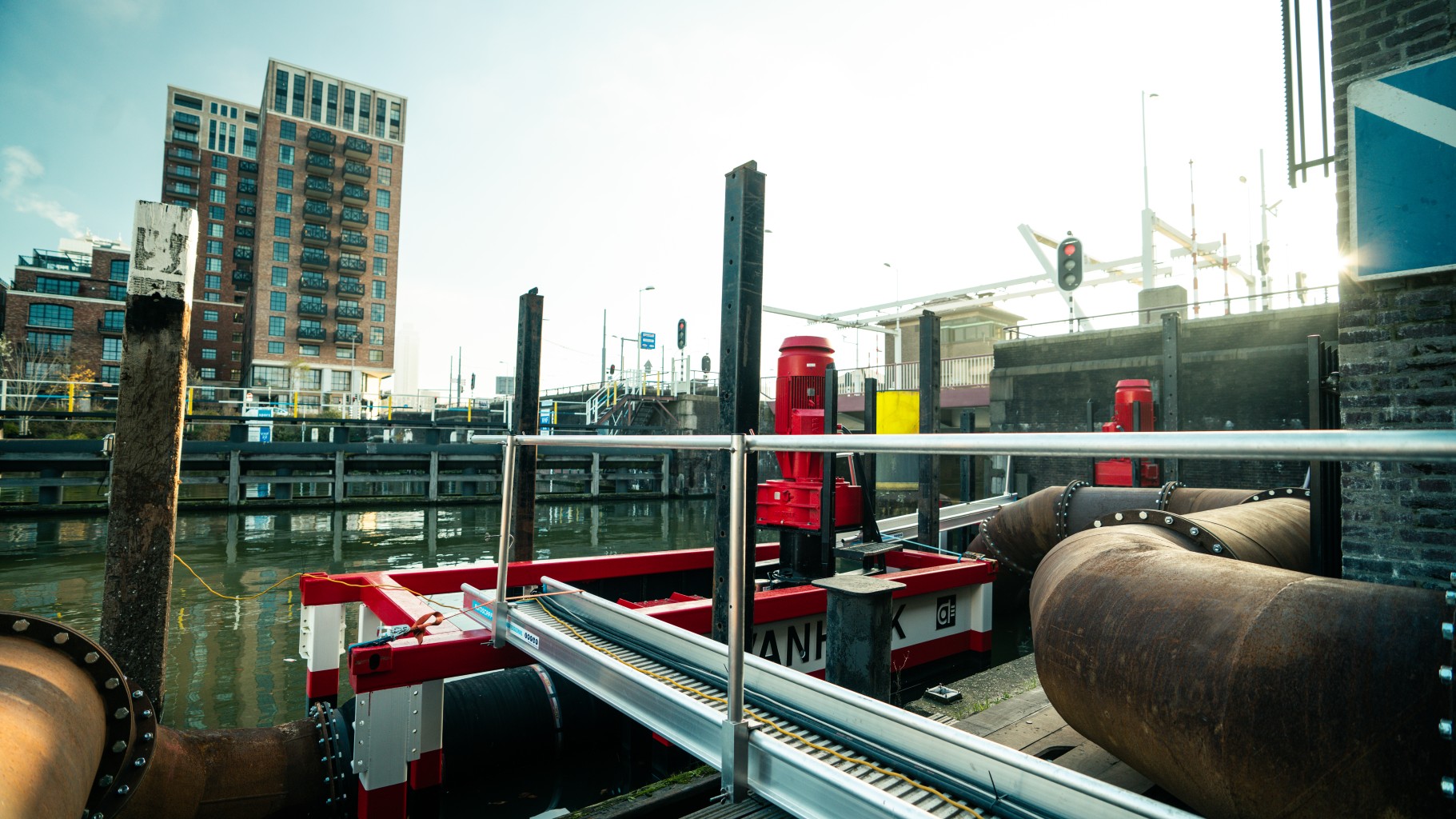 Twee VP800's bij gemaal Parksluizen Twee pompsets staan in het water nabij een sluis met leidingwerk. Op de achtergrond staat aan de overkant van het water een woontoren