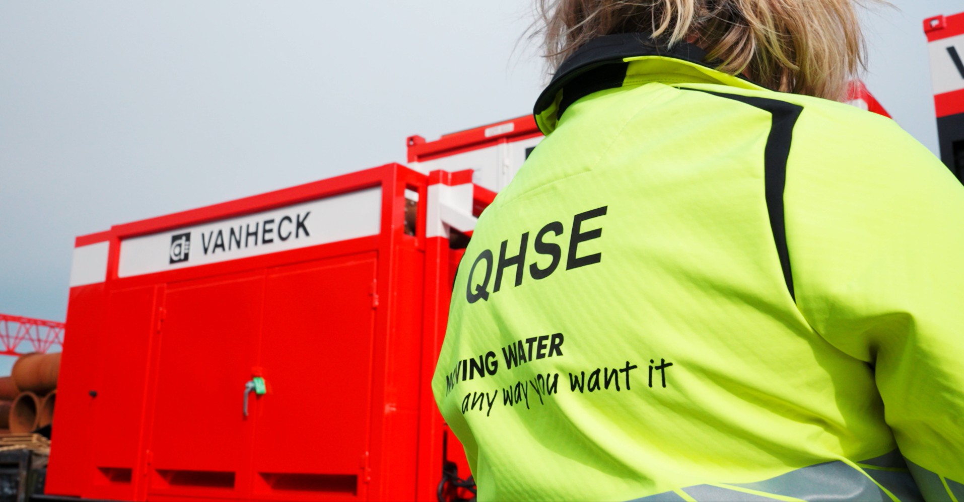 Collega in gele signaaljas met QHSE erop, naast een rood equipment
