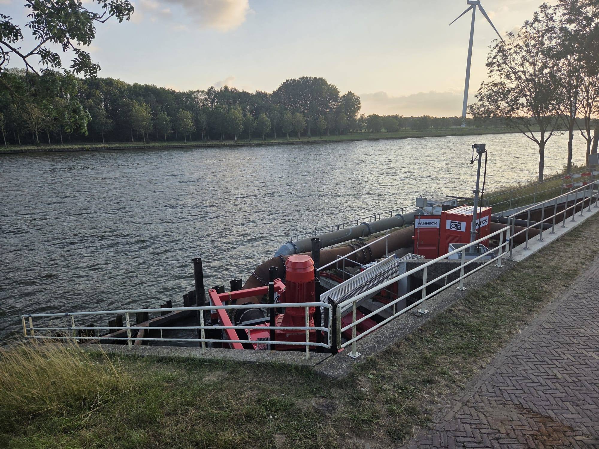 Rood equipment naast de kade langs een kanaal met aan weerszijden een bomenrij