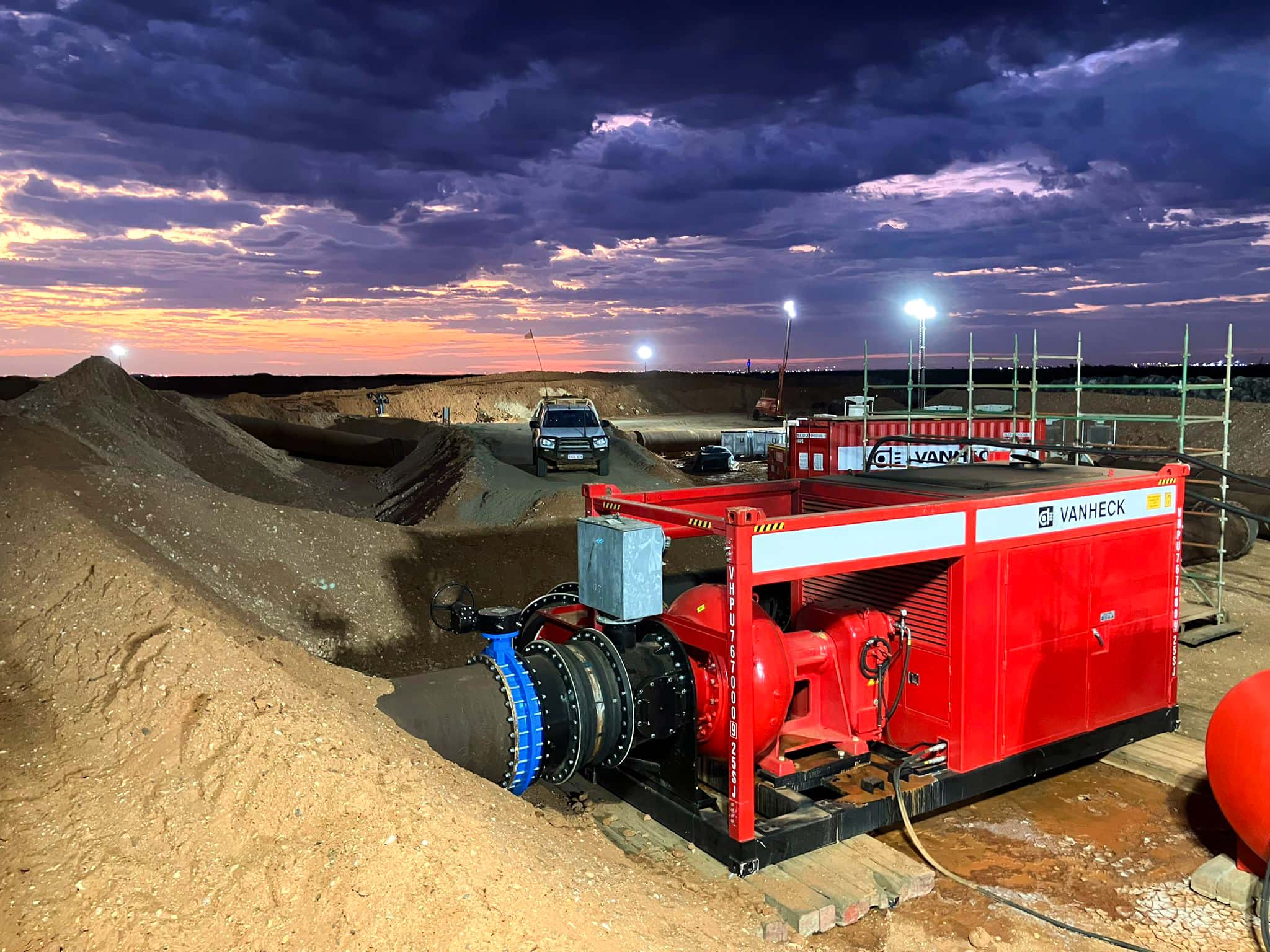 Red returnwaterpump on a construction site at sunset, with a truck in the background and dramatic clouds in the sky.