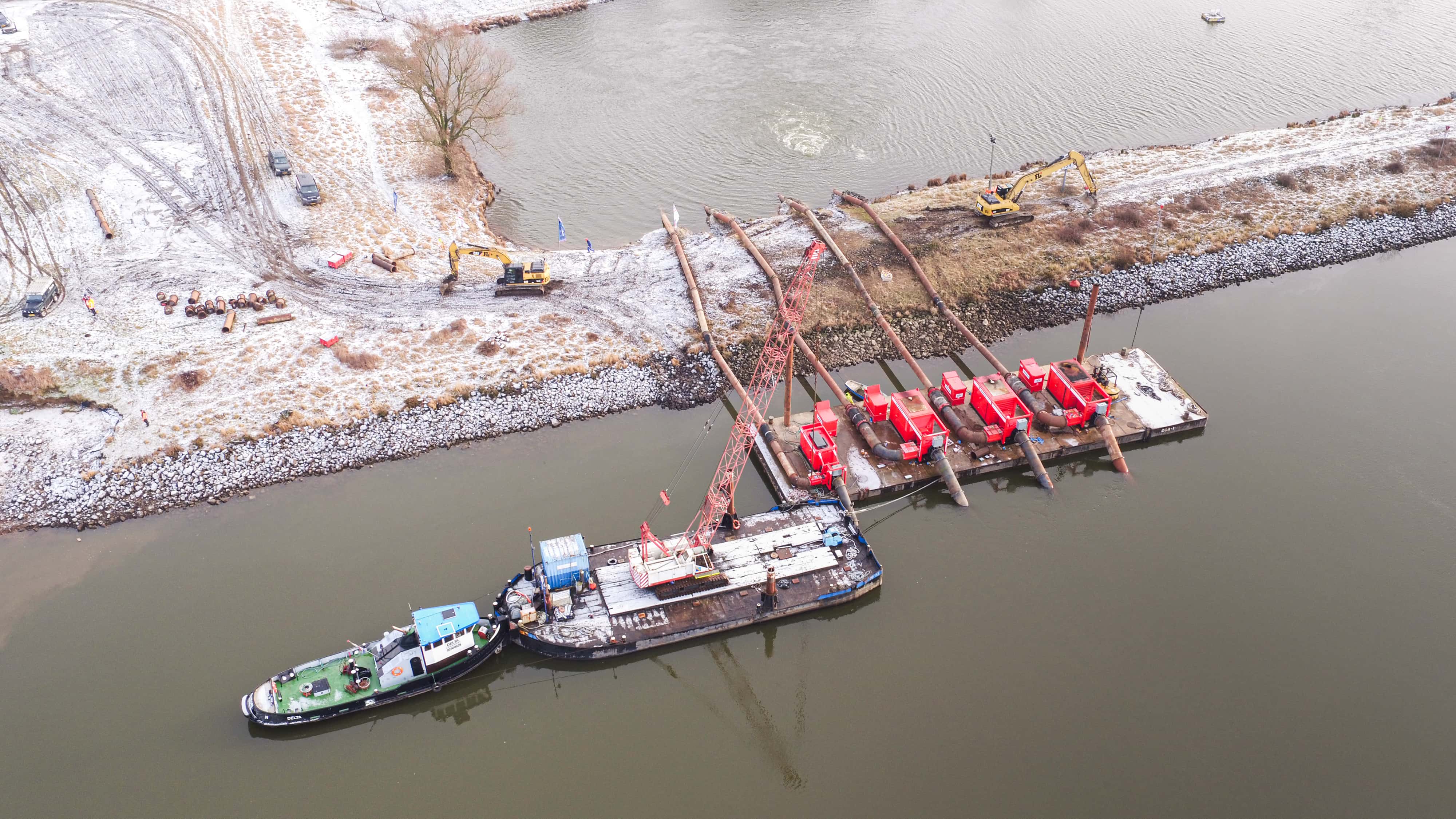 Luchtfoto noodpompinstallatie Luchtfoto van een rivier met daarin een duwboot, boot met kraan en een ponton met daarop 4 rode waterpompen met 4 leidingen naar een ander water. Op de dijk staan twee graafmachines