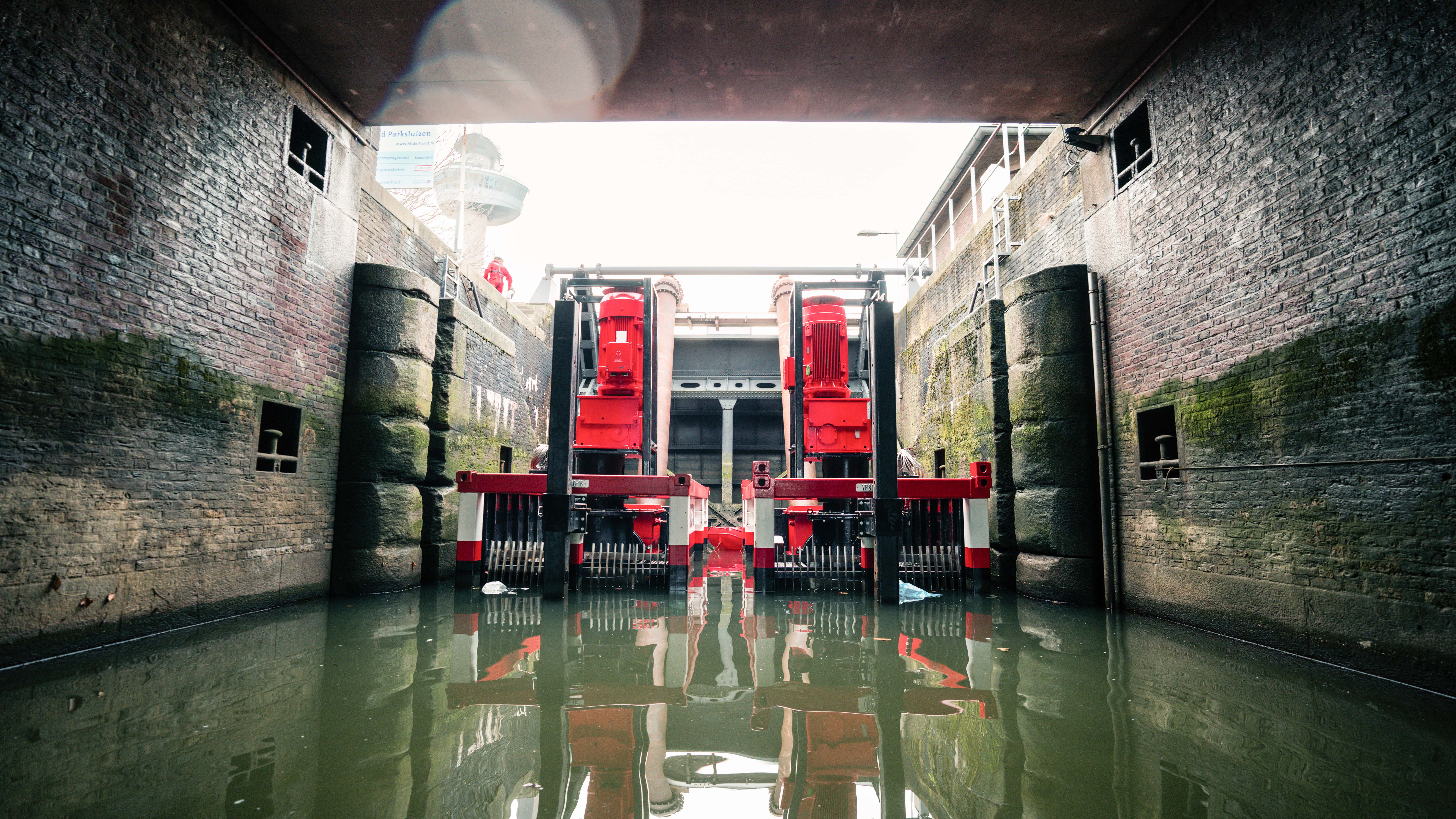 Twee VP800's in een sluis twee grote rood-witte containers staan in het water in een sluis met bakstenen muren. Twee grote rode elektromotoren staan bovenop de pompsets. op de achtergrond is een sluisdeur te zien en een grote toren.