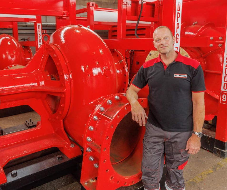 Een collega in werkkleding staat geleund op een grote rode pomp