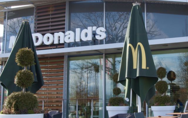 Outdoor seating area at a McDonalds restaurant with green umbrellas and potted plants.